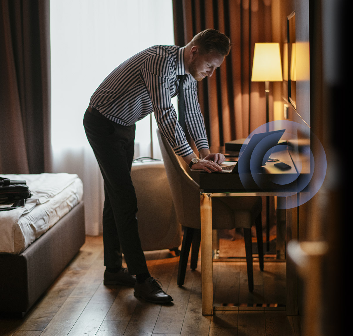 A man using a mobile hotspot to connect to a laptop on a desk inside a hotel.