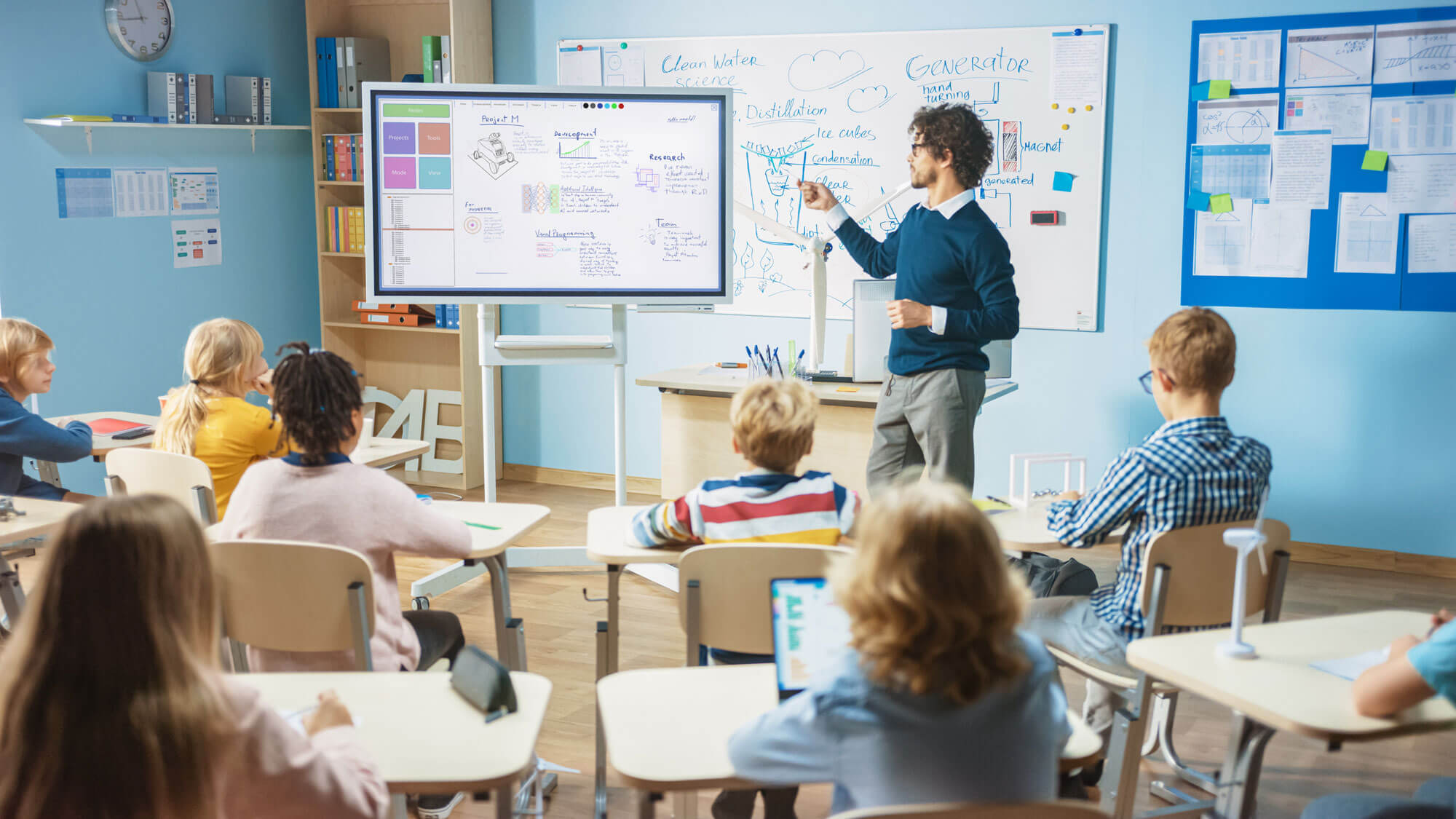 Classroom teacher using an interactive whiteboard to teach pupils using devices.